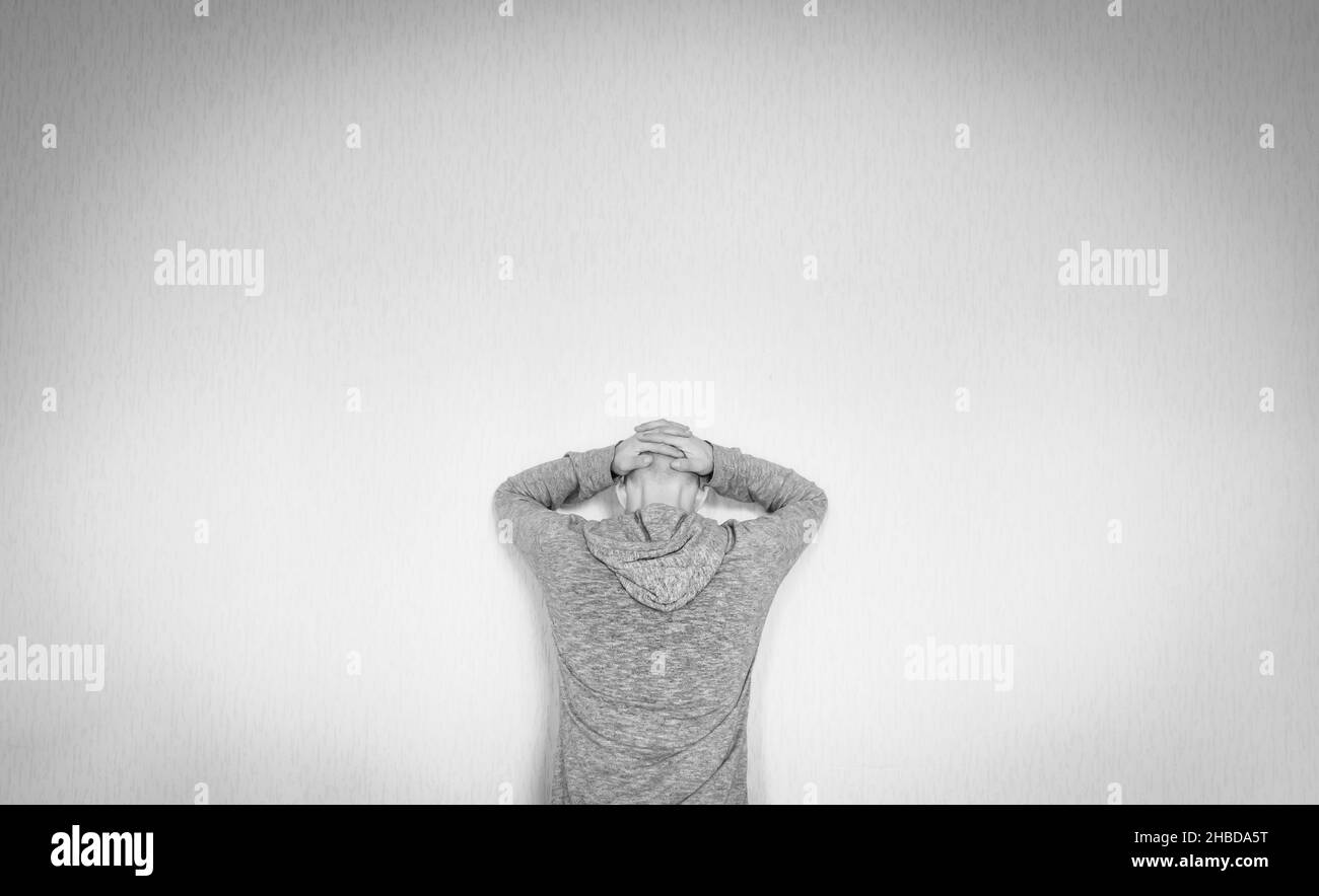 La persona maschio in felpa con cappuccio è appoggiata verso il muro con le mani sulla testa rasata. Concetto di decompressione e ritiro personale. Foto Stock