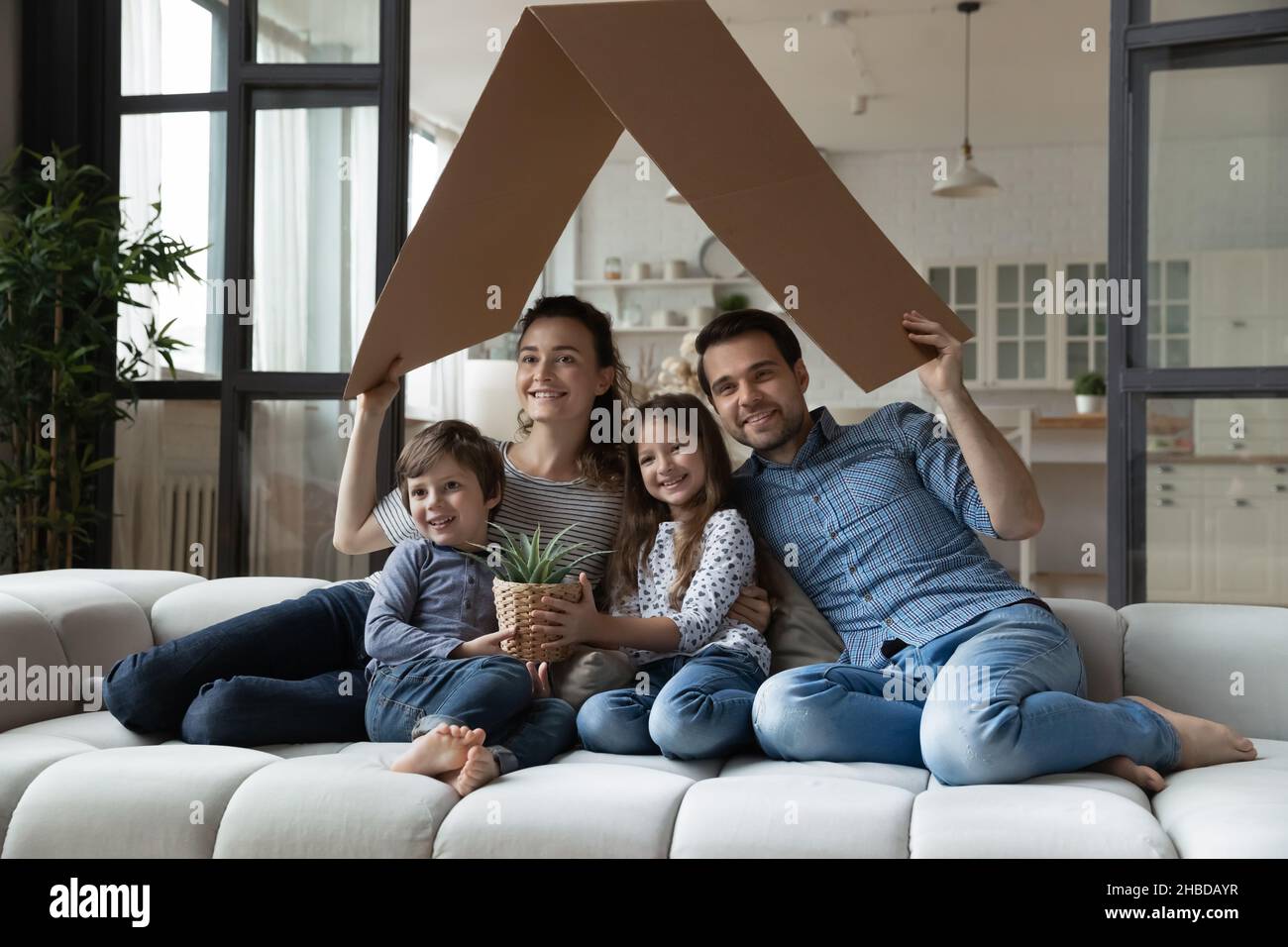 Famiglia felice con i bambini seduti sul divano sotto il tetto di cartone Foto Stock