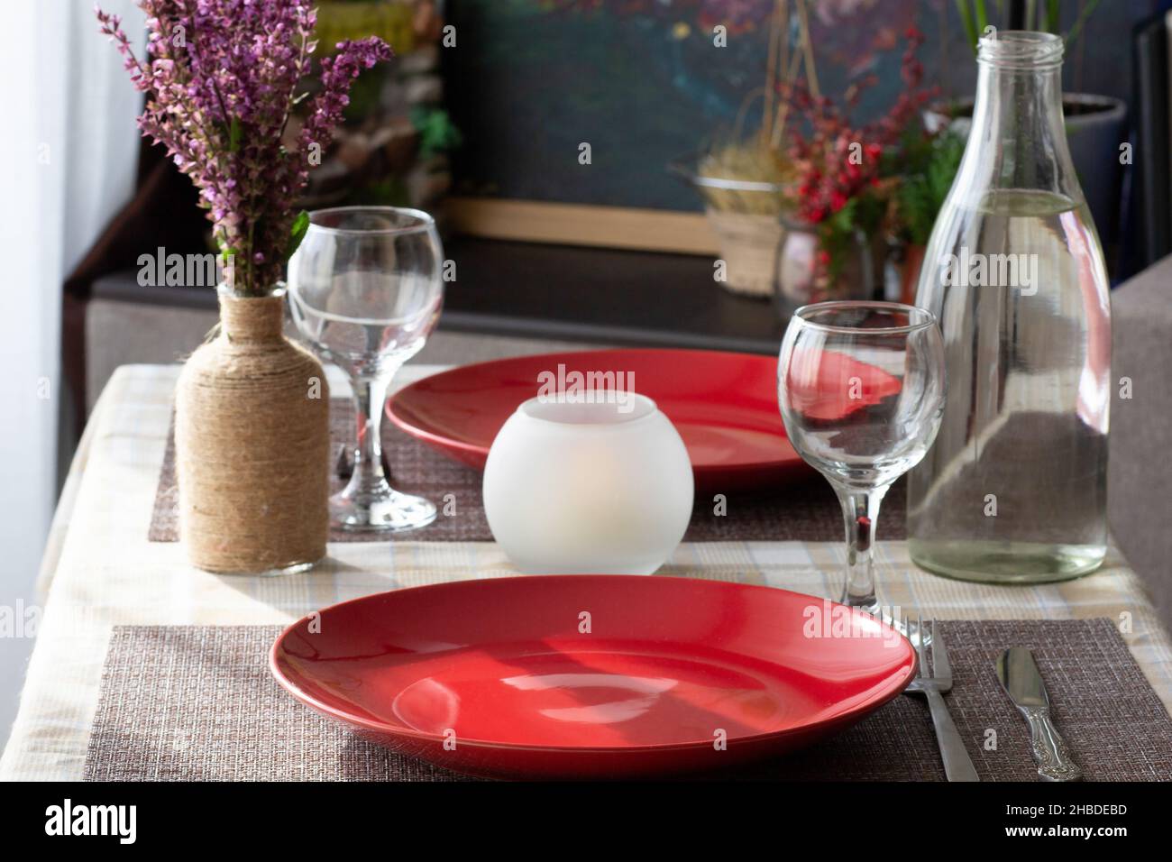 Tavolo con stoviglie: Vuoto senza pasto piatti rossi, bicchieri da vino, bottiglia d'acqua e coltello e forchetta per cena romantica per due persone a casa Foto Stock
