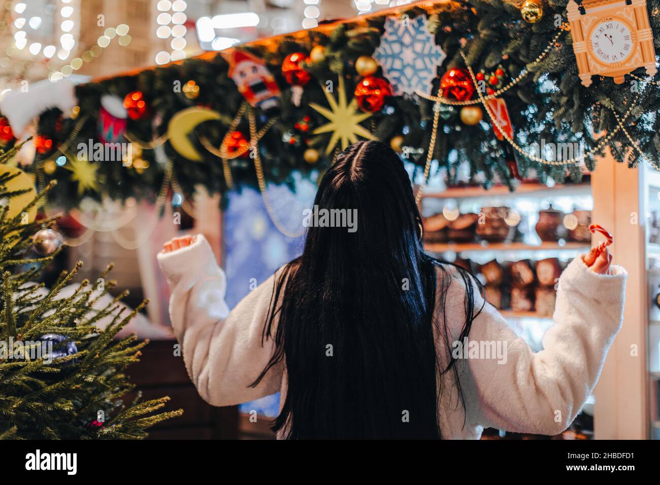 Giovane donna brunetta in pelliccia bianca invernale alla fiera di Natale con decorazioni magiche dorate Foto Stock