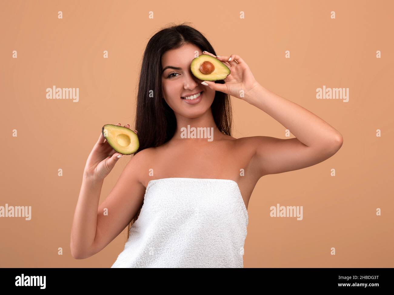Bella signora armena avvolto in asciugamano che copre l'occhio con metà di avocado su sfondo beige studio Foto Stock