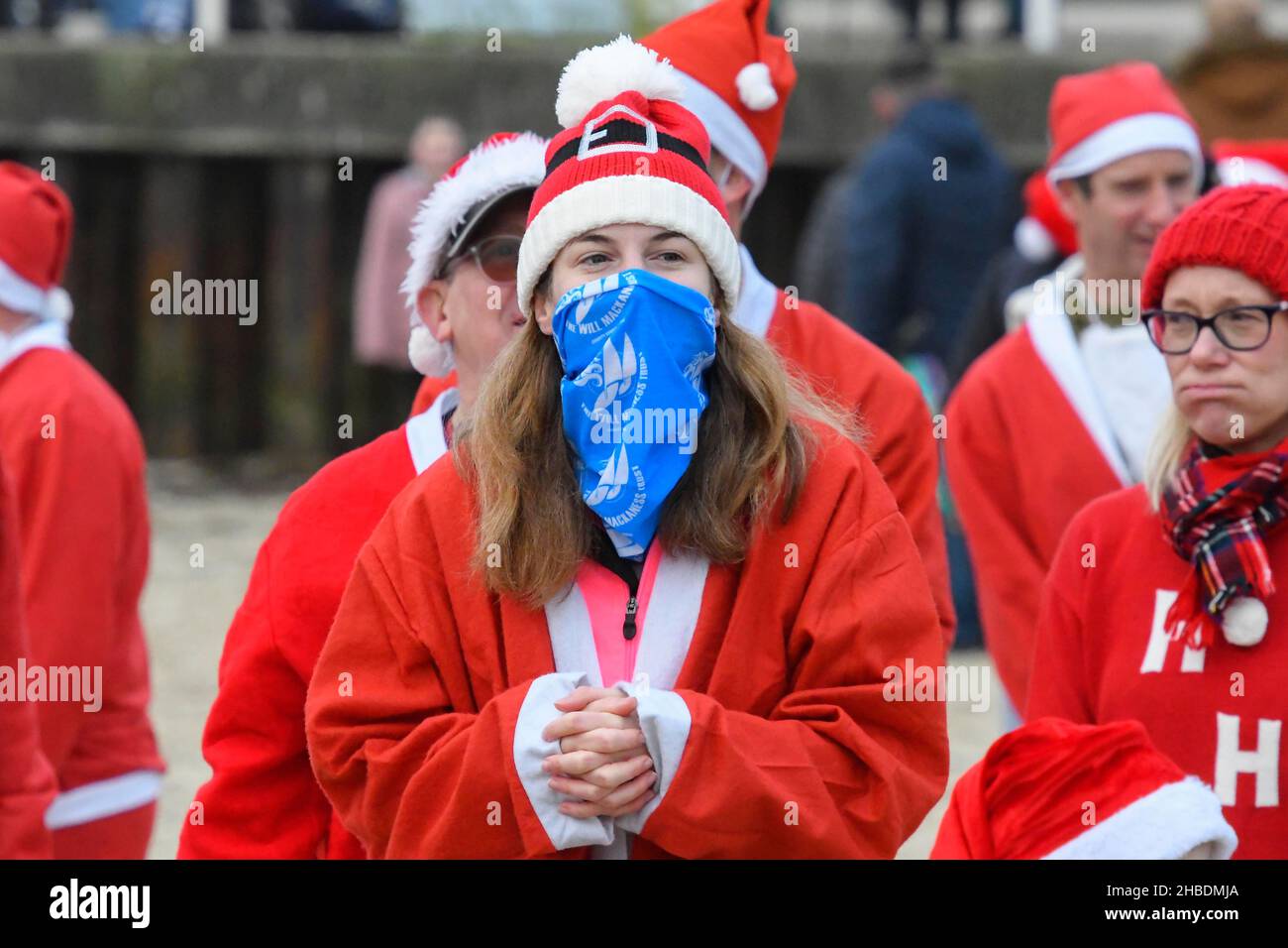 Weymouth, Dorset, Regno Unito. 19th dicembre 2021. Centinaia di corridori vestiti come Babbo Natale prendono parte all'annuale The Chase the Pudding pre-chistmas correre sulla spiaggia di Weymouth nel Dorset. L'evento annuale sta raccogliendo fondi per la carità Mackaness fiducia. Corridore che indossa una maschera facciale. Picture Credit: Graham Hunt/Alamy Live News Foto Stock