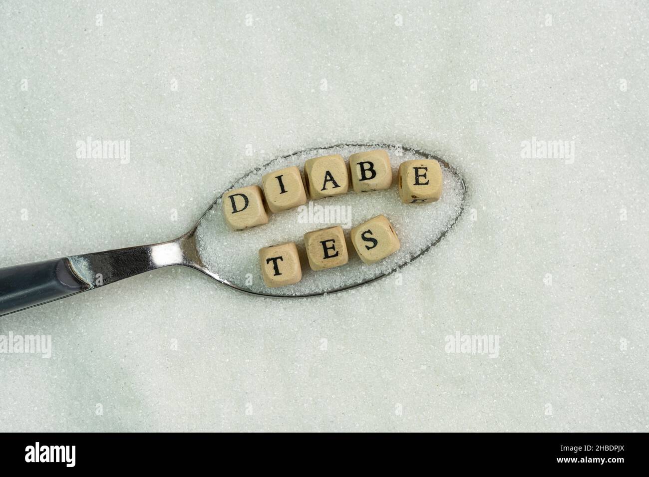 La parola diabete all'interno di un cucchiaio pieno di zucchero Foto Stock