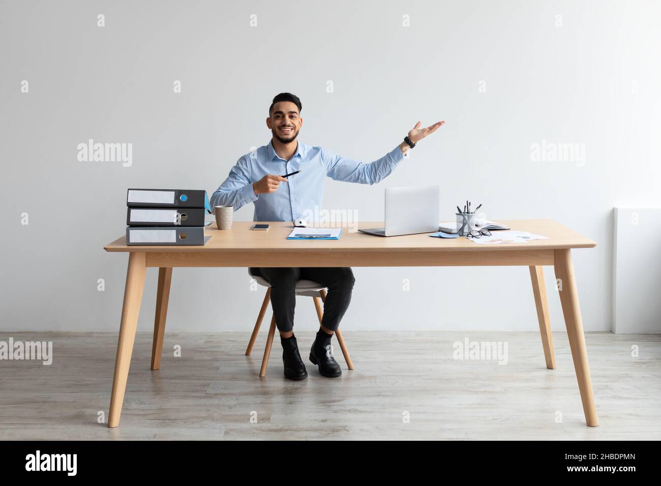 Uomo d'affari felice che punta da parte seduto al posto di lavoro Foto Stock