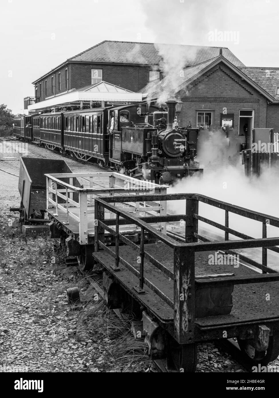 Un treno lascia la stazione di Tywyn Wharf alla ferrovia di Talyllyn, Gwynedd, Galles in primo piano sono i camion che sono stati utilizzati per il trasporto dell'ardesia Foto Stock