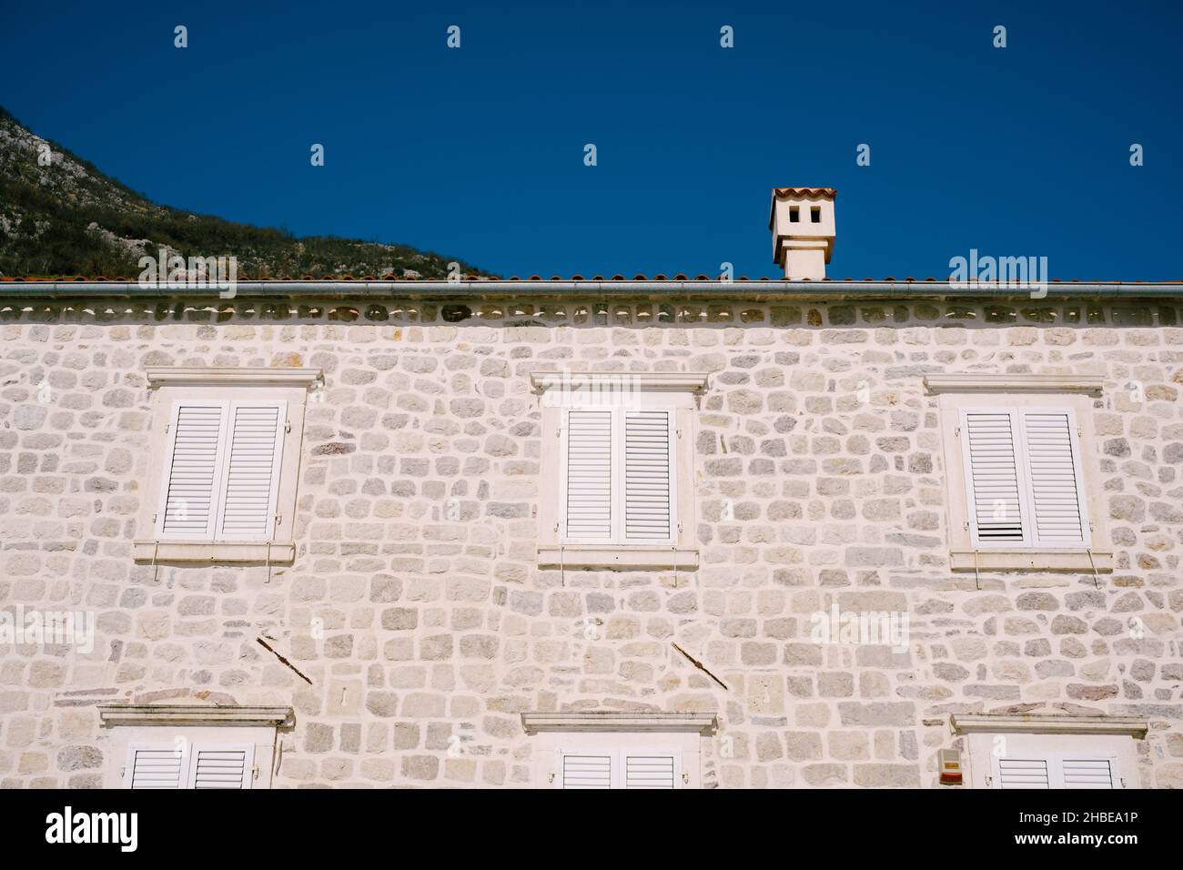 Facciata dell'edificio in pietra grigia con persiane bianche sulle finestre Foto Stock