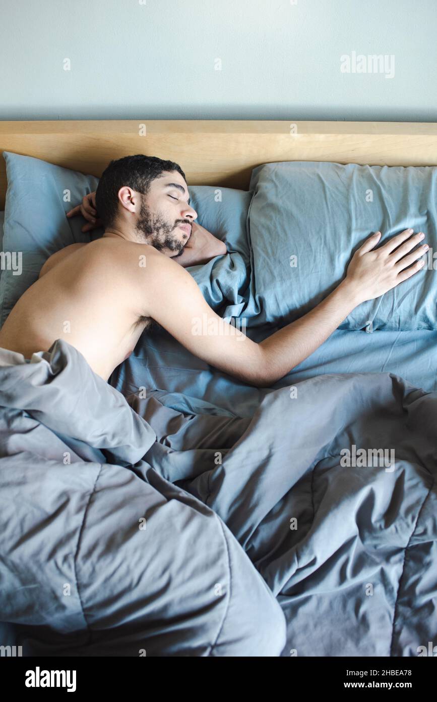 Multirazziale sottile uomo milleniale con barba che dorme con mano sul cuscino, partner mancante, singolo o nuovo uomo al mattino Foto Stock