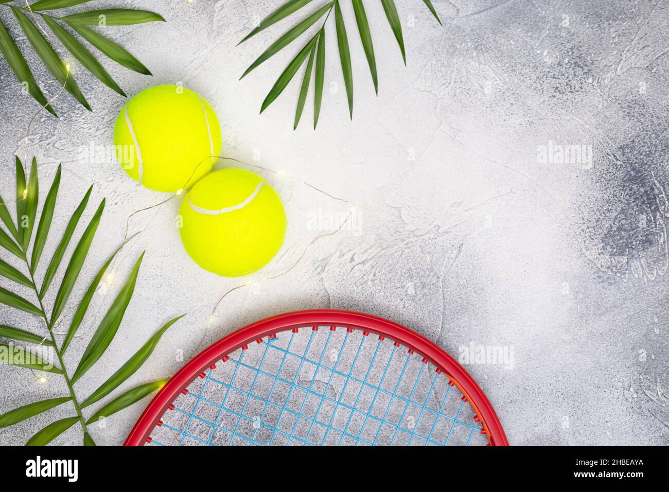 Tennis. Composizione sportiva con palle da tennis con racchetta e foglie di palma su sfondo blu con spazio per la copia. Sport e stile di vita sano. La conce Foto Stock
