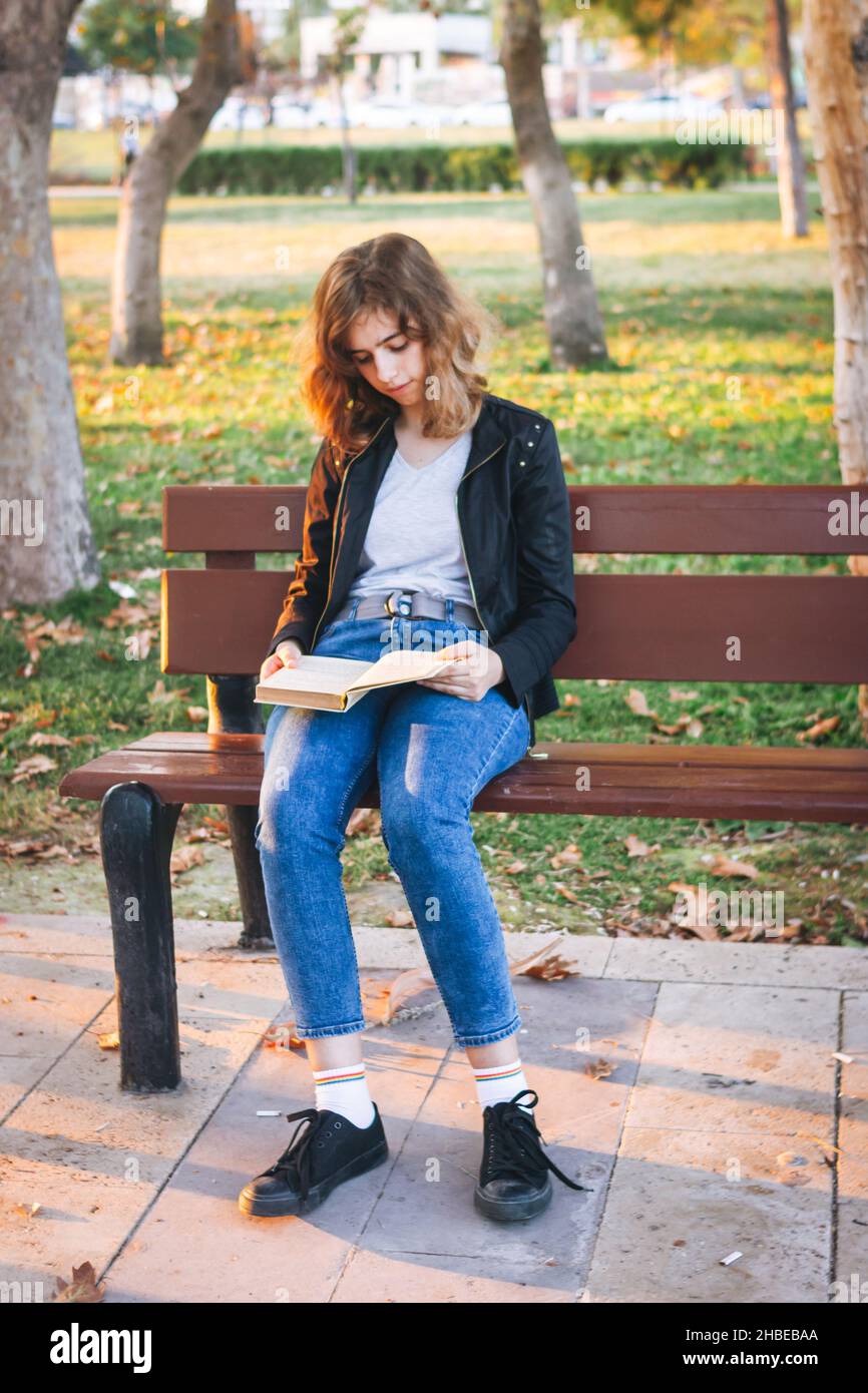 Ragazza allegra che legge libro su panchina al parco autunnale Foto Stock