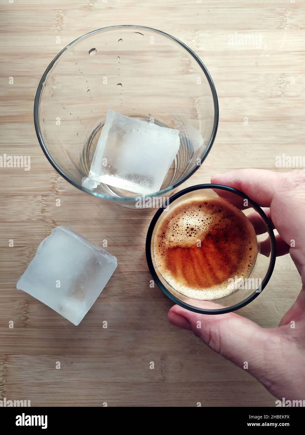 Donna che sta per versare una dose di caffè espresso in un bicchiere con un cubetto di ghiaccio per preparare il caffè ghiacciato Foto Stock