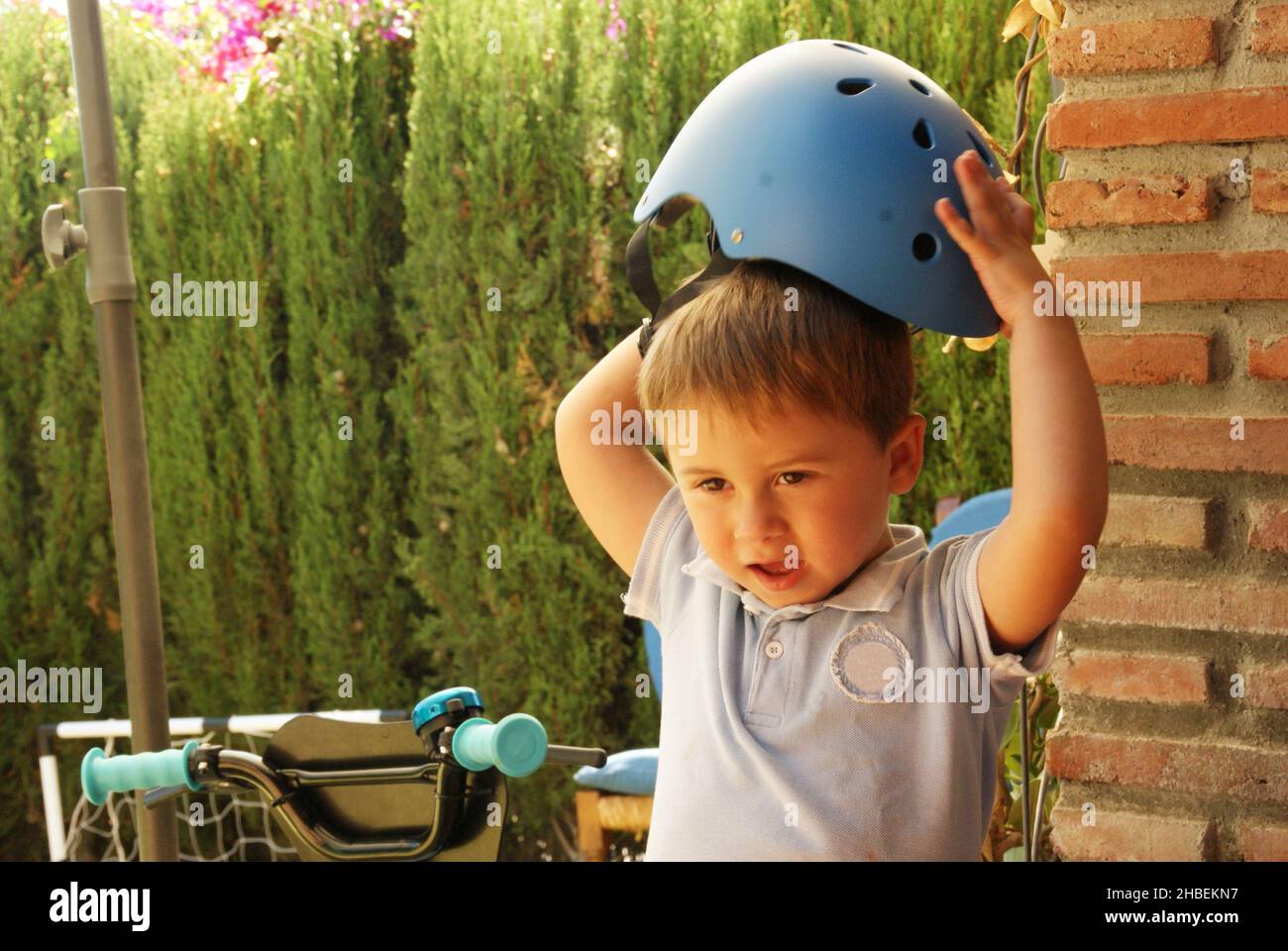 Ragazzo in piedi in un giardino mettendo su un casco da ciclismo Foto Stock