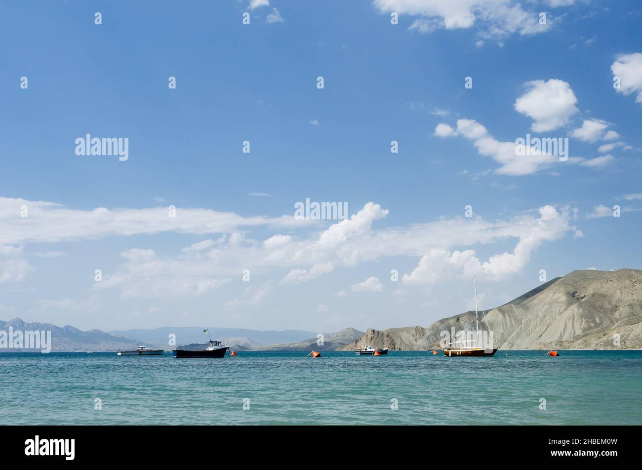 Resort estivo sul mare. Cielo blu con nuvole di cumulo. Paesaggio soleggiato con barche sull'acqua. Montagne all'orizzonte Foto Stock