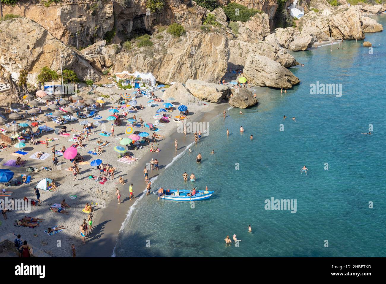 Pescatori in barca da pesca tipica lasciando Calahonda spiaggia affollata di Beach goers. Nerja, Costa del Sol, Provincia di Malaga, Andalusia, Spagna meridionale. Foto Stock
