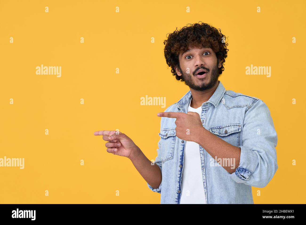 Stupito sorpreso giovane indiano che punta su sfondo giallo. Foto Stock