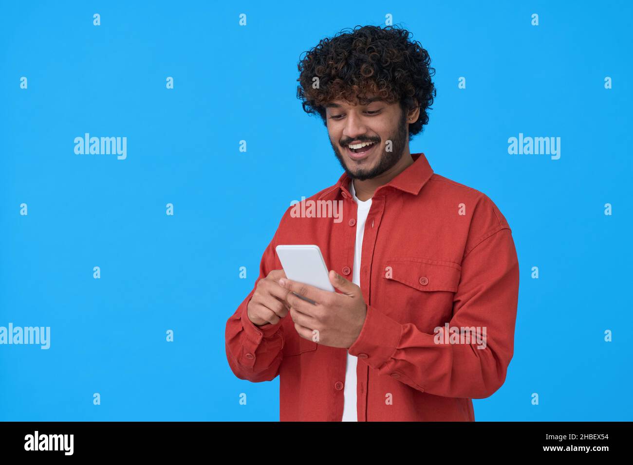 Felice uomo indiano giovane utilizzando il telefono cellulare isolato su sfondo blu. Foto Stock