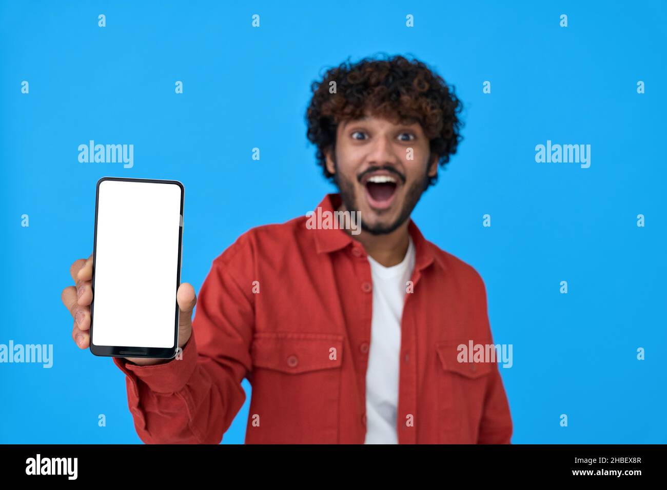 Il giovane indiano eccitato che tiene il cellulare mostrando grande schermo bianco mockup. Foto Stock