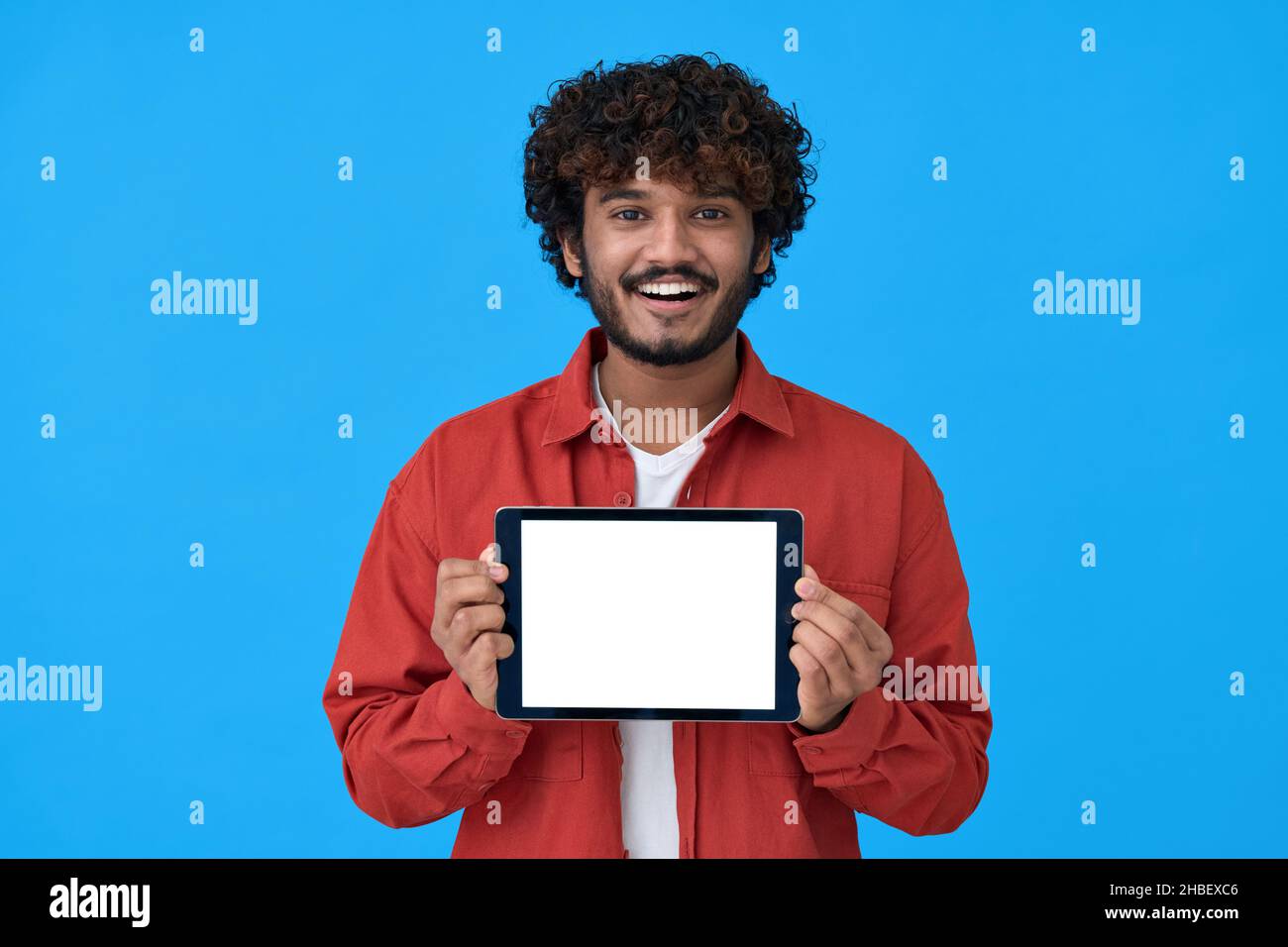 Felice giovane uomo indiano che mostra grande schermo mockup tablet su sfondo blu. Foto Stock