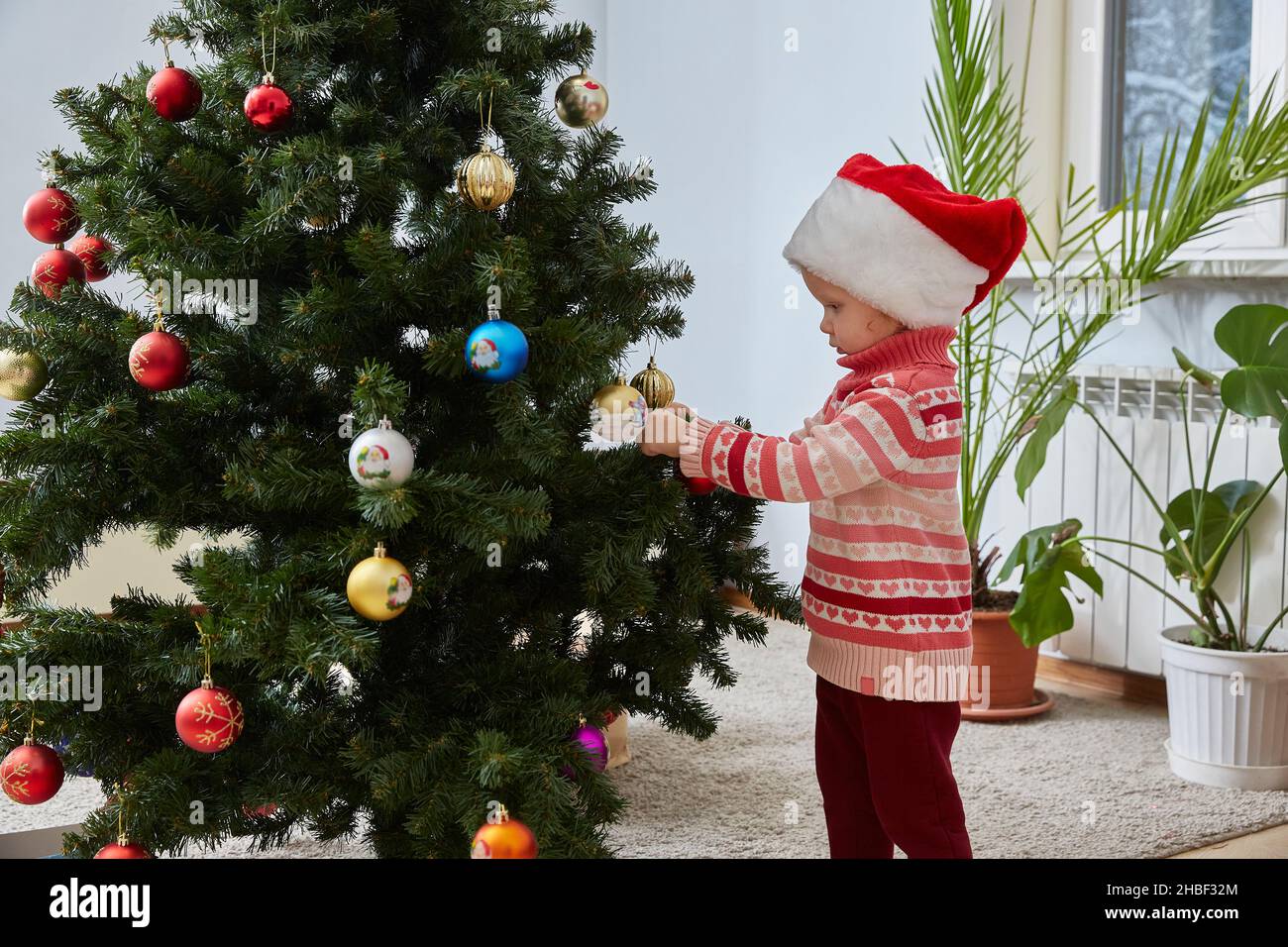 Ragazza in un cappello di Babbo Natale si veste un albero di Natale. Foto Stock