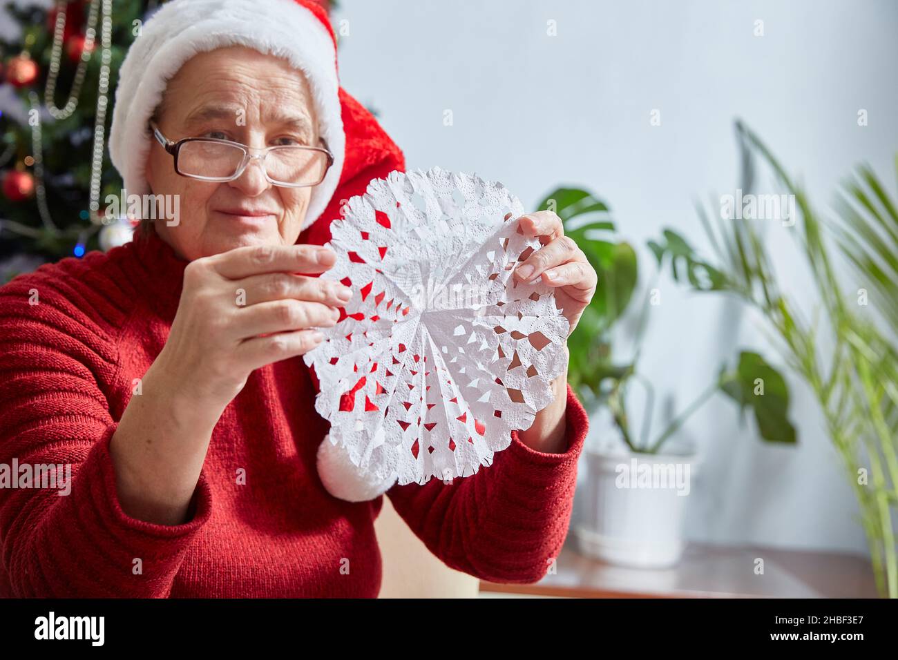donna anziana tiene un fiocco di neve tagliato di carta nelle sue mani. Decorazione per il nuovo anno e Natale. Foto Stock