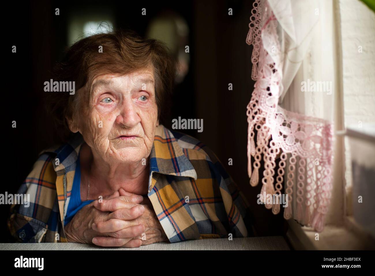 Una donna anziana siede pensierosamente alla finestra. Foto Stock