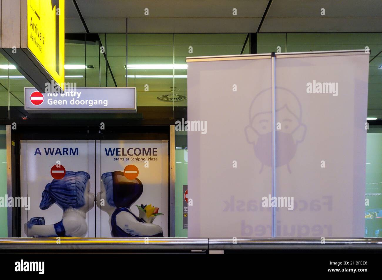 Aeroporto Internazionale Schiphol, Amsterdam, Paesi Bassi: Cartello "un caloroso benvenuto" con figure bissanti, con un cartello che invita a indossare una maschera Foto Stock