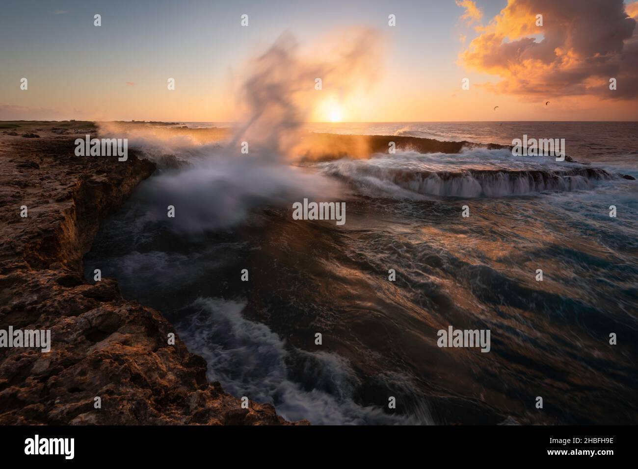 Le onde si infrangono in una grotta marina mentre l'acqua spara nell'aria come uno spruzzo di nebbia salata lungo la costa settentrionale di Aruba. Foto Stock