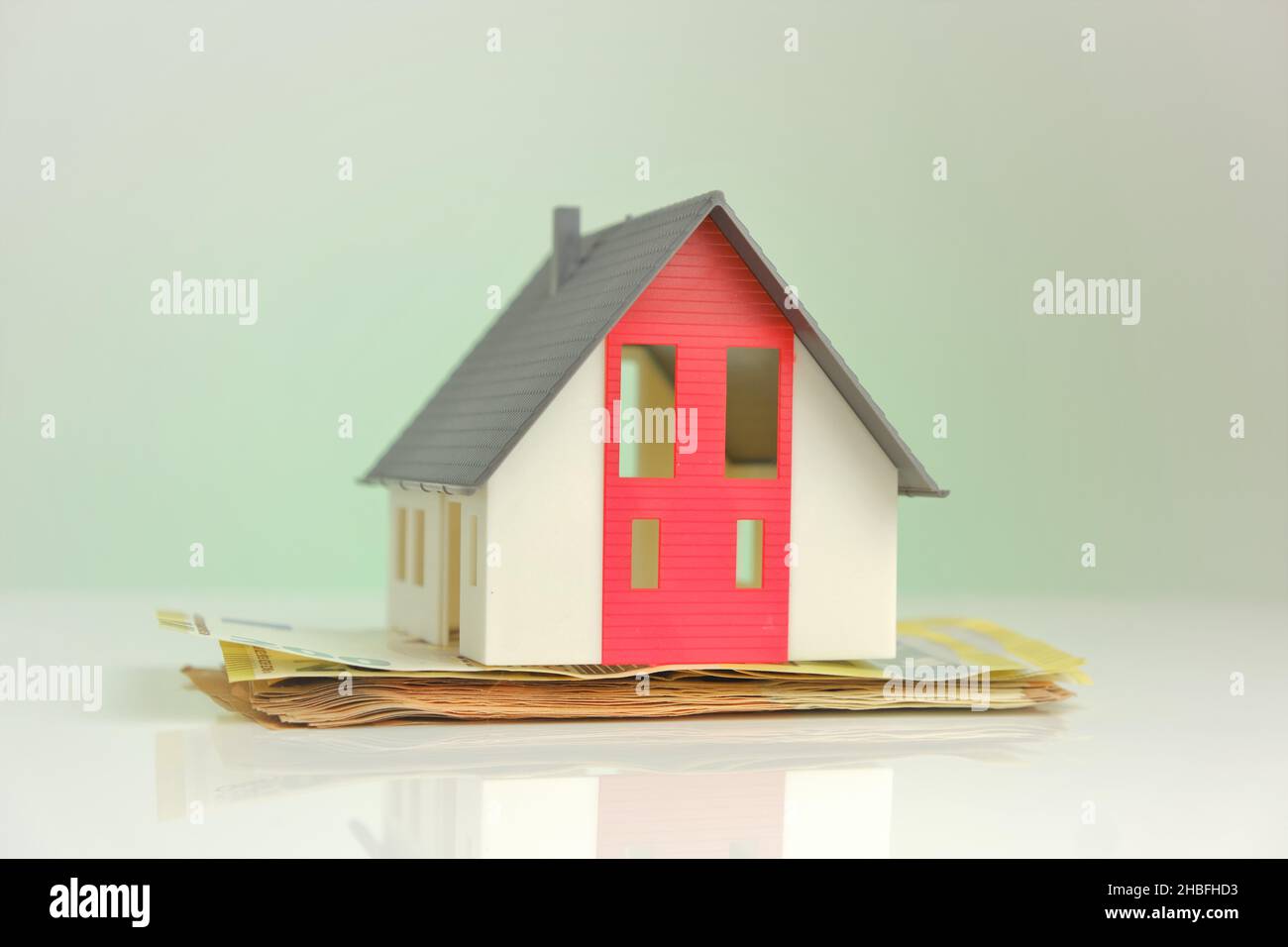 Acquisto e costruzione di una casa. Casa e soldi. Casa mock con tetto su sfondo banconote in euro. Mercato immobiliare. Prestito immobiliare. Foto Stock