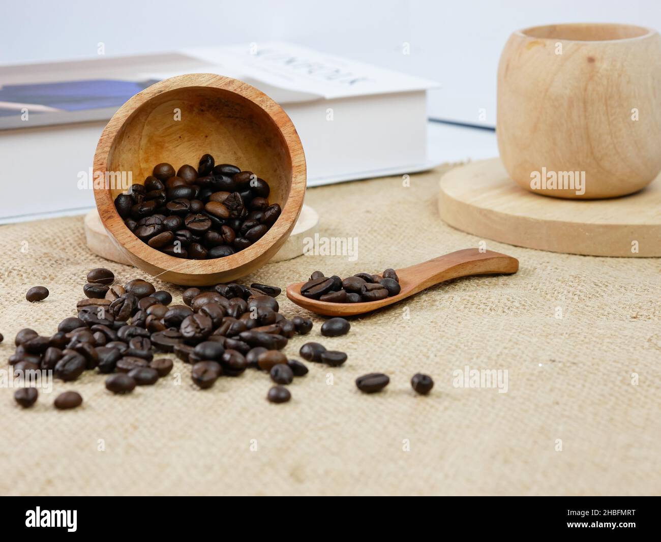 Tazza di caffè in legno con chicchi di caffè e libro con sfondo sfocato. Attività mattutine Foto Stock