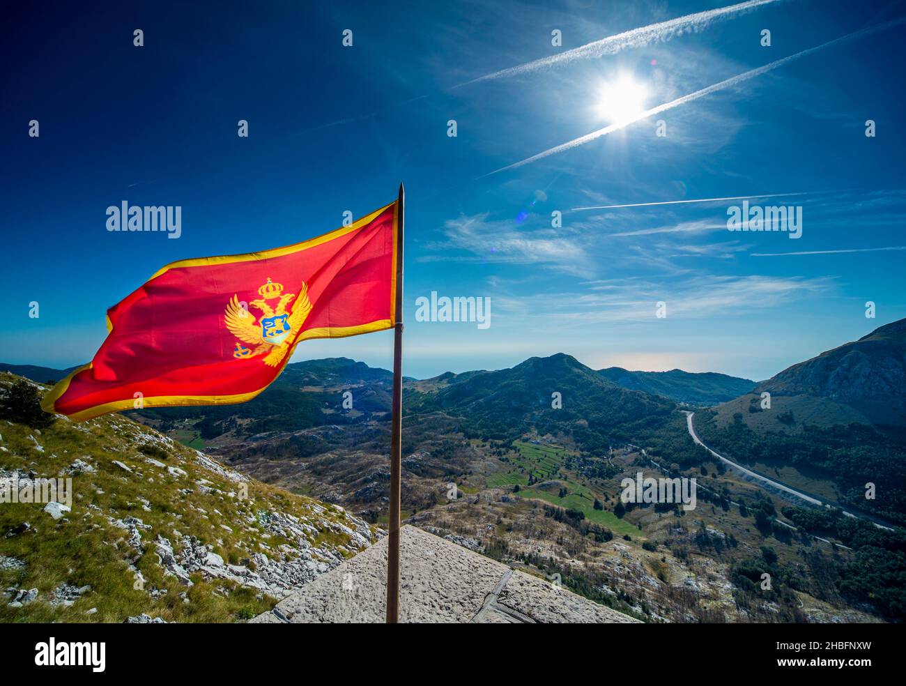 Sulla cima del monte Lovcen, la maestosa bandiera nazionale rossa dello stato balcanico che sbatte nel vento, contro cieli limpidi e soleggiati blu di fine estate Foto Stock