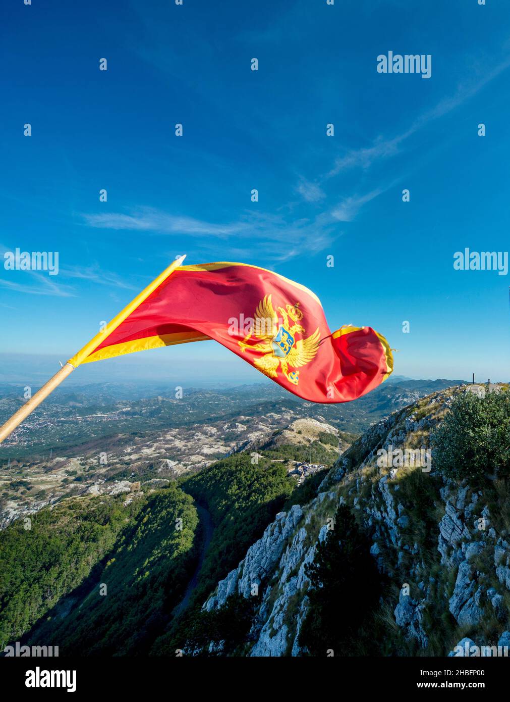 Sulla cima del monte Lovcen, la maestosa bandiera nazionale rossa dello stato balcanico che sbatte nel vento, contro cieli limpidi e soleggiati blu di fine estate Foto Stock