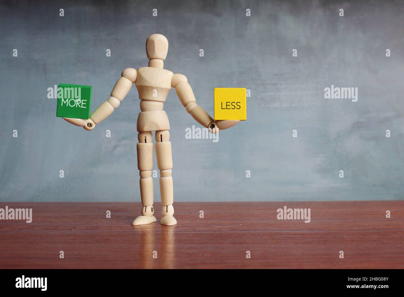 Figura umana in legno che bilancia cubi in legno con testo SEMPRE MENO. Foto Stock