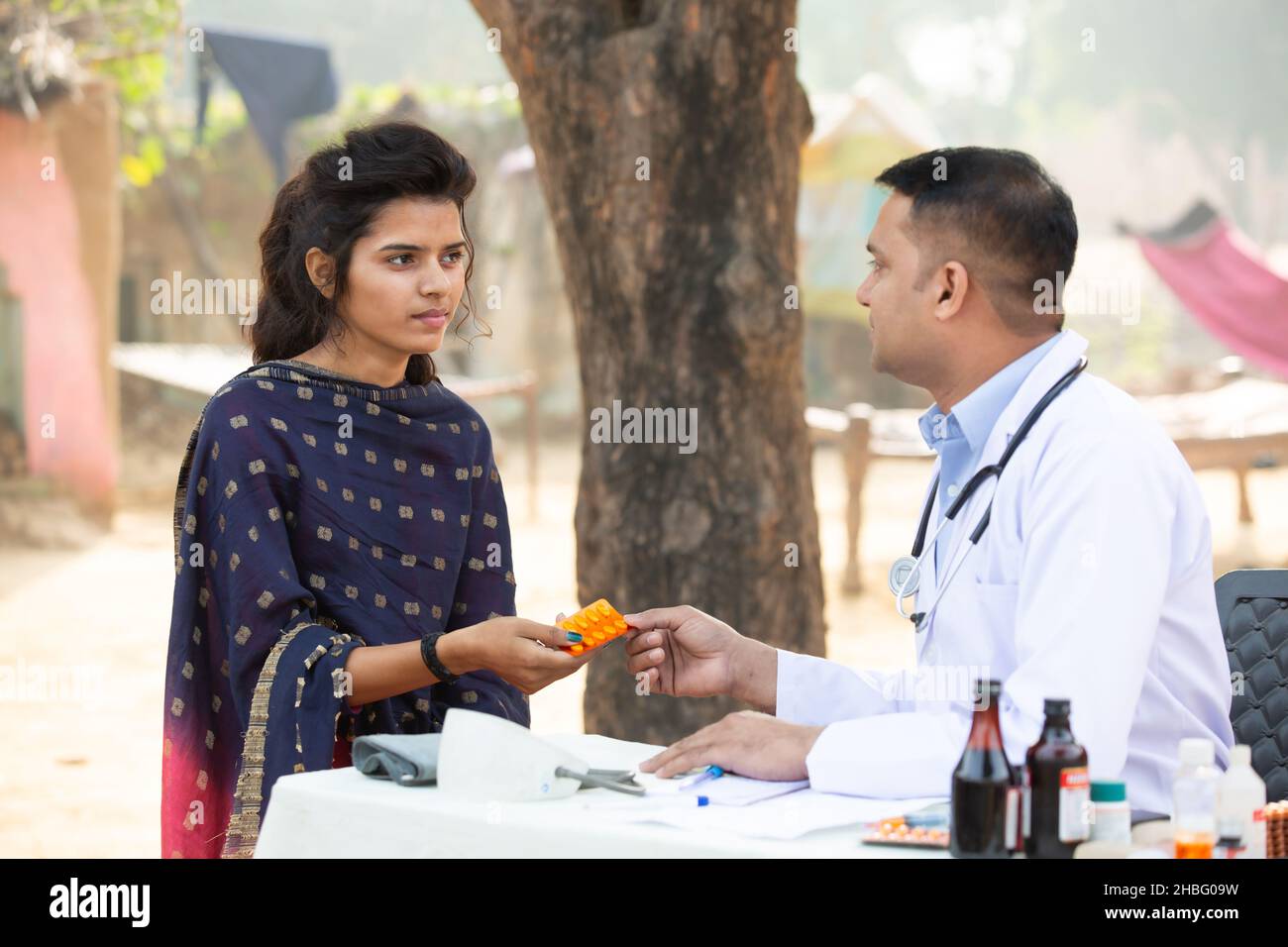 Medico indiano maschio dare medicina alla giovane ragazza adulta al villaggio, donna ottenere tablet droga da persona medica all'aperto. Sanità rurale india. Foto Stock