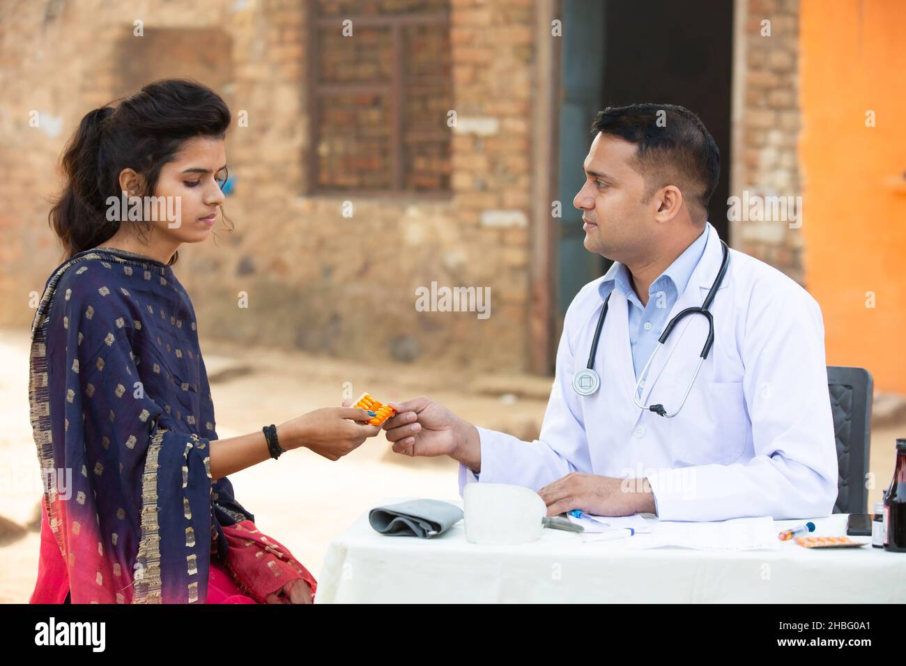 Medico indiano maschio dare medicina a giovane paziente adulto in villaggio, donna ottenere tablet droga da persona medica all'aperto. Sanità rurale india. Foto Stock