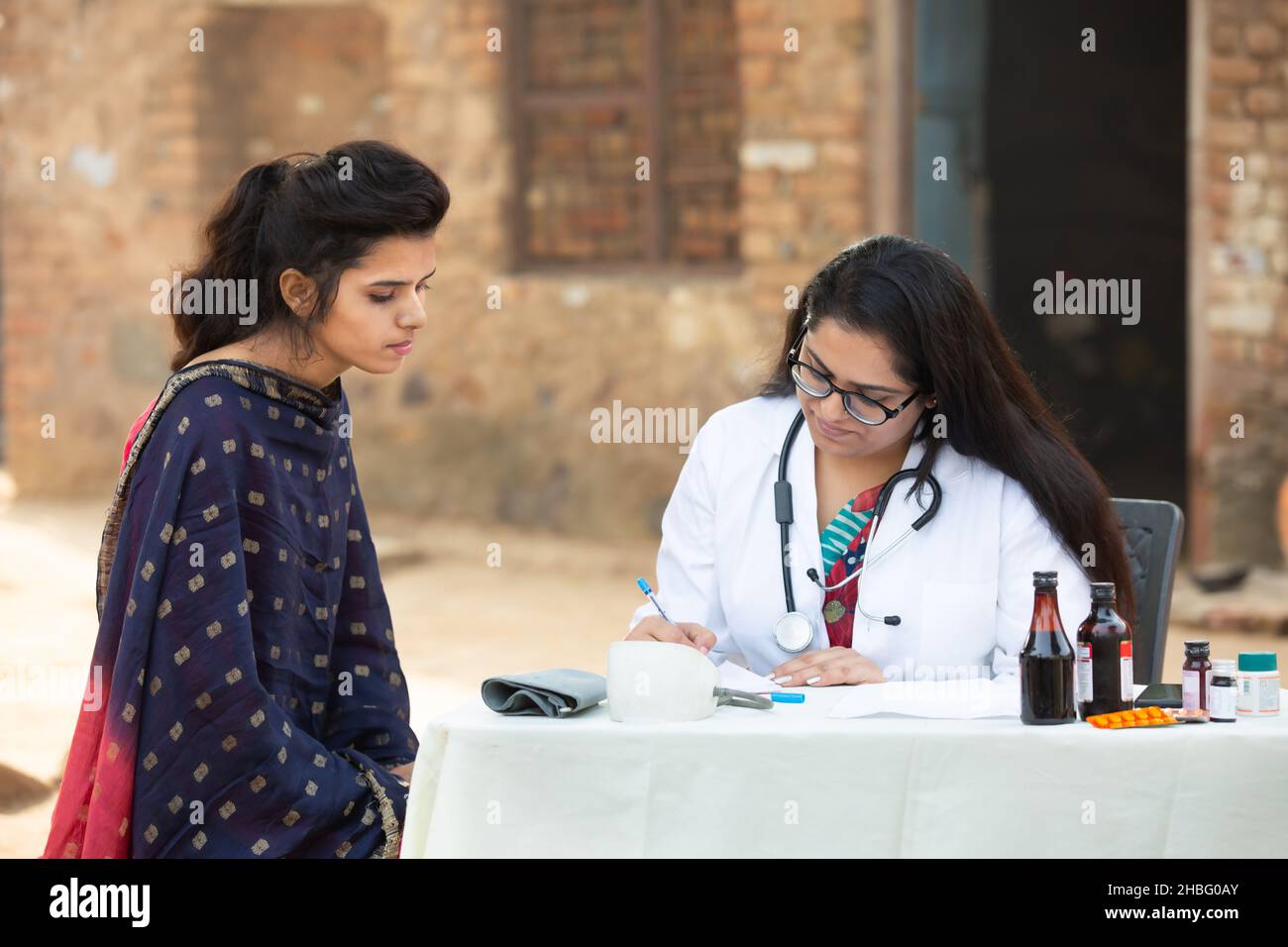 Medico indiano femmina che scrive la prescrizione di medicina al paziente giovane della ragazza adulta al villaggio all'aperto, donna di preoccupazione che ottiene l'esame da persona medica, Rur Foto Stock