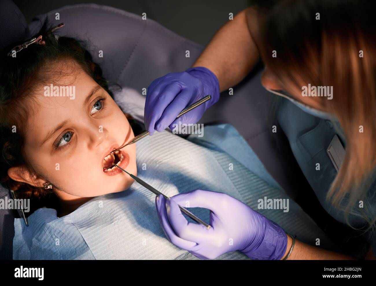 Primo piano di ragazza con bocca aperta guardando il dentista mentre la donna controlla i denti del bambino. Dentista che esamina i denti del bambino con esploratore dentale e specchio. Concetto di odontoiatria pediatrica e cura dentale. Foto Stock