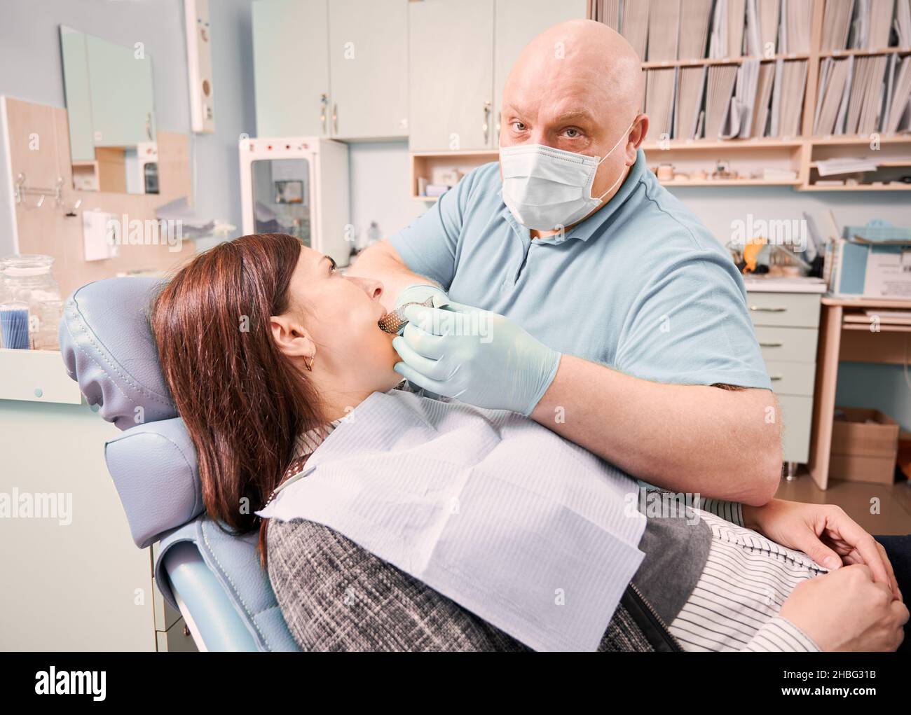 Dentista maschile che esegue la procedura dentale nel moderno centro medico. Paziente sdraiato in sedia dentale durante il trattamento stomatologico. Concetto di odontoiatria, stomatologia e cura dentale. Foto Stock