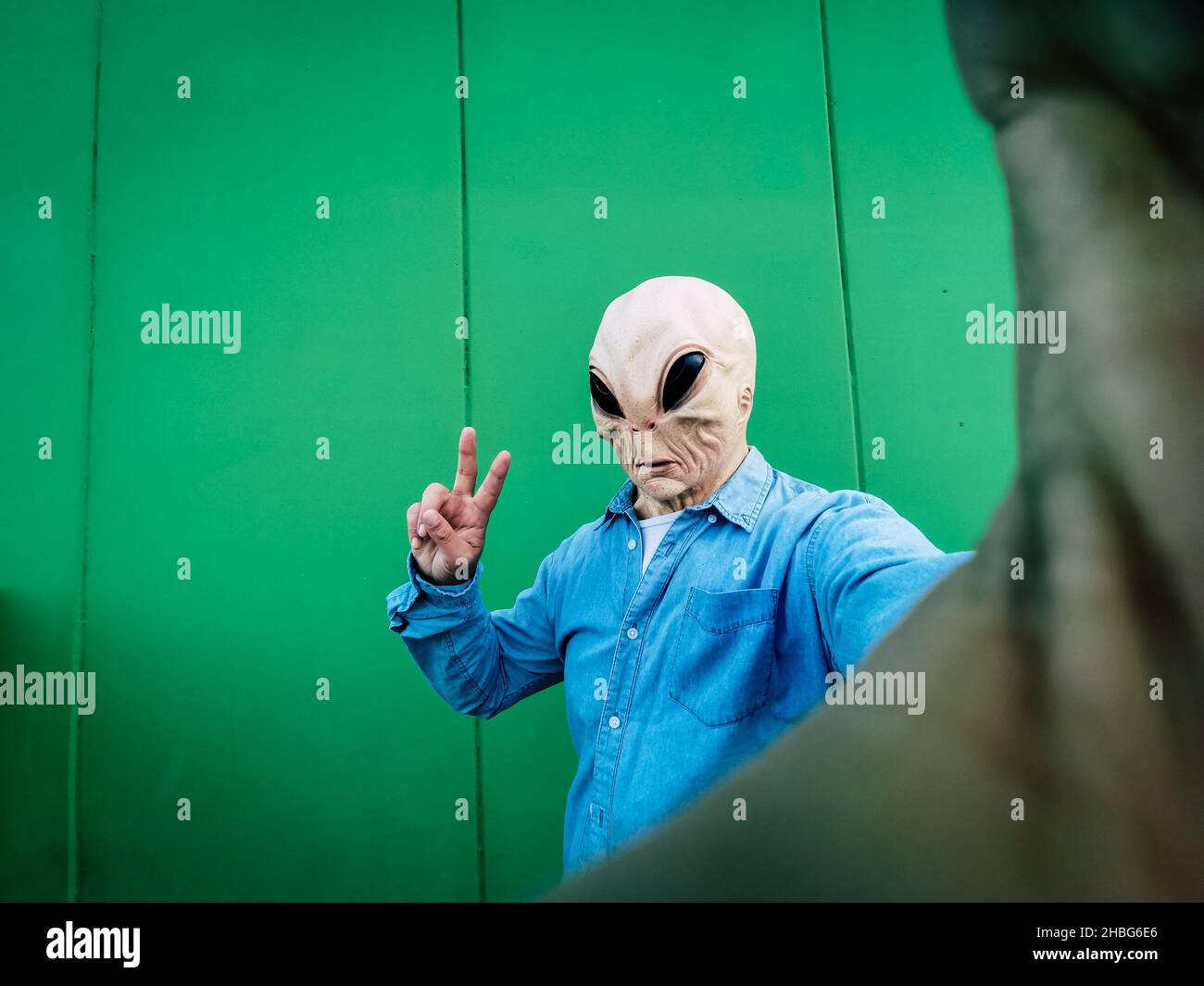 Maschera aliena in piedi faccia scattare foto selfie contro la parete di sfondo verde. Copia spazio per divertente fumetto pubblicità. UFO incasuale extraterrestre de Foto Stock