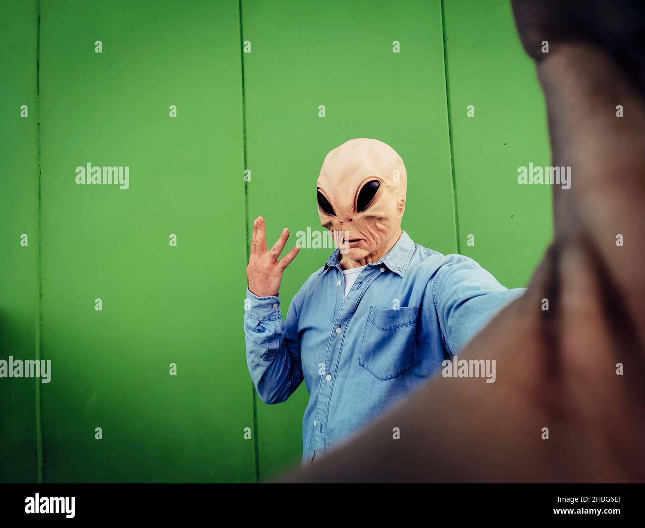 Maschera aliena in piedi faccia scattare foto selfie contro la parete di sfondo verde. Copia spazio per divertente fumetto pubblicità. UFO incasuale extraterrestre de Foto Stock