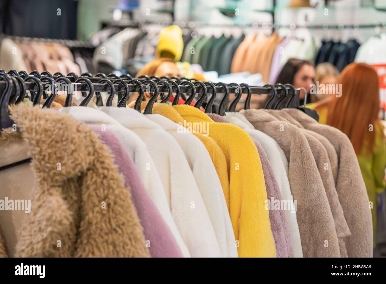 Moda pelliccia faux cappotti appesi sul rack in negozio di abbigliamento, vari colori, fuoco selettivo, sfondo sfocato di interni del negozio, ragazze, clienti Foto Stock