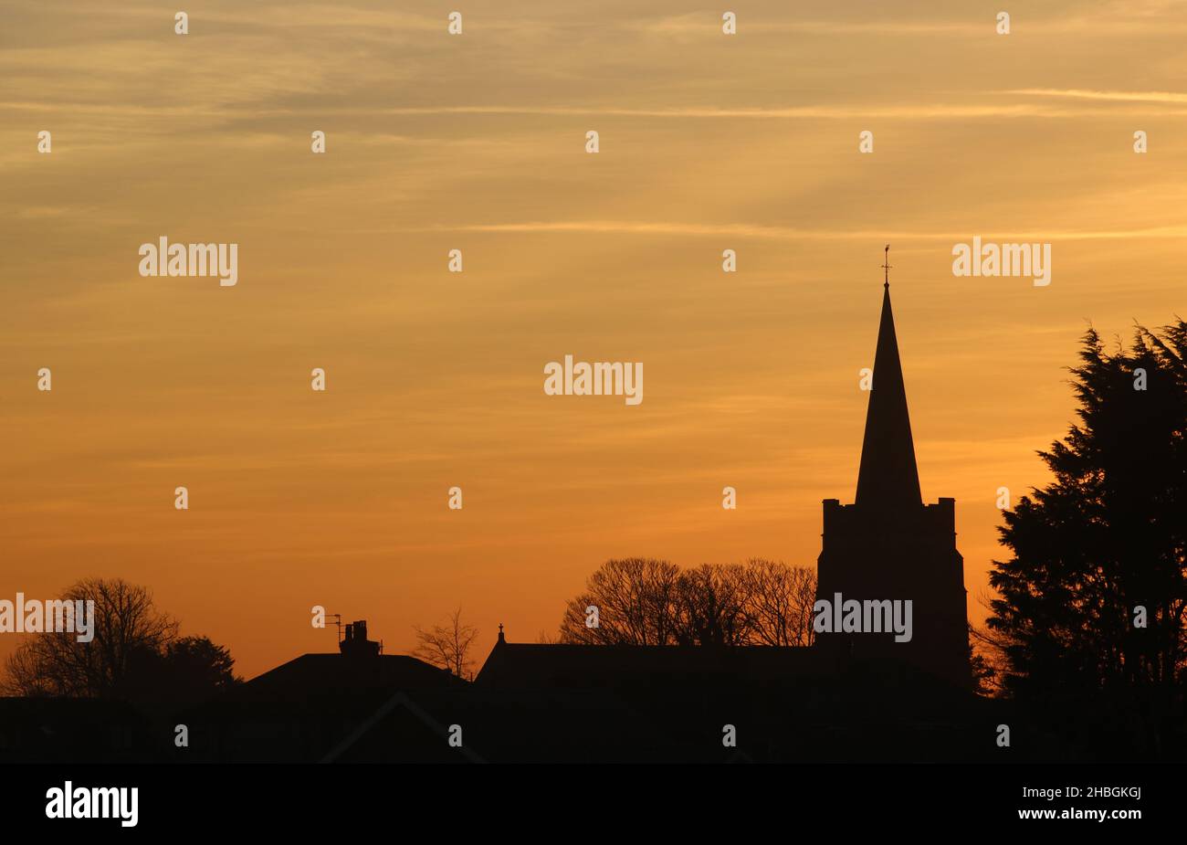 Silhouette di alberi, tetti e torre e campanile della Chiesa di San Giovanni Battista a Pilling, Lancashire al tramonto una sera di dicembre. Foto Stock