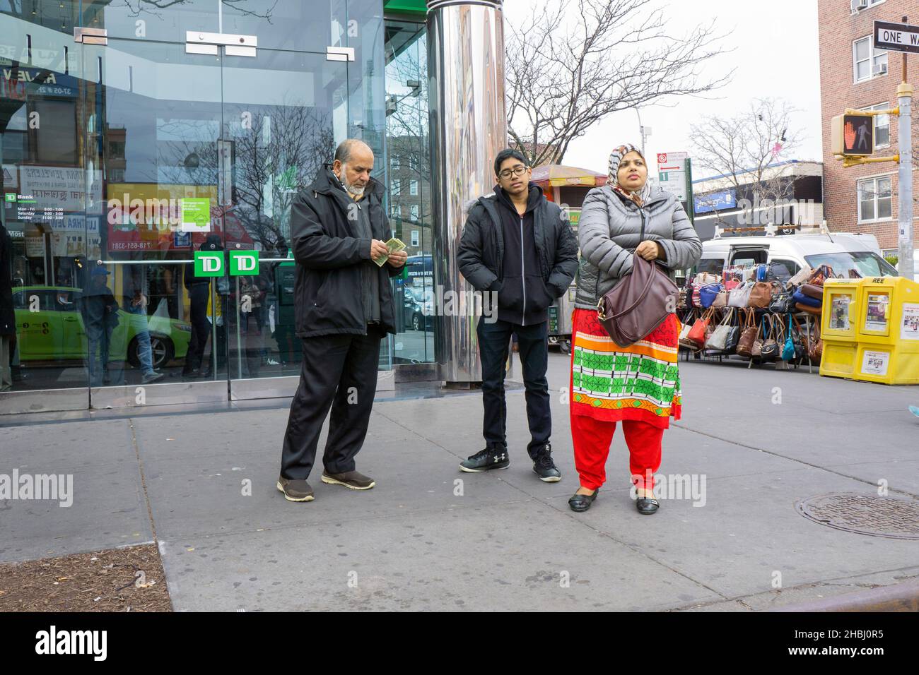 Una famiglia musulmana lascia la propria banca locale con il padre contando i suoi soldi ritirati. A Jackson Heights, Queens, New York City. Foto Stock