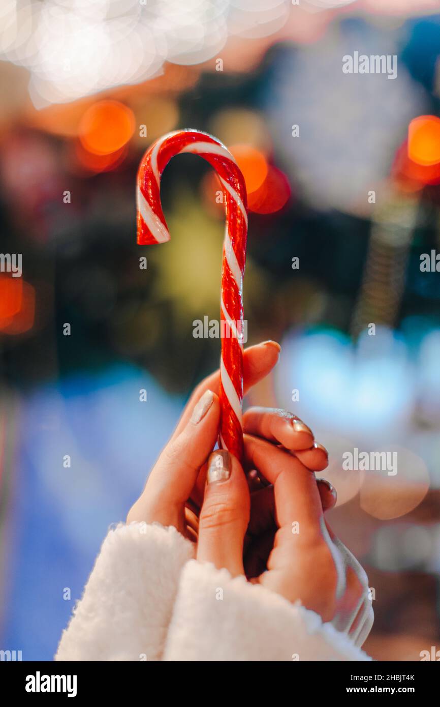 Le mani femminili che tengono rosso bianco canna dolce lecca lecca lecca caramella contro lo sfondo della luce blu bokeh. Dettagli fata di Natale Foto Stock