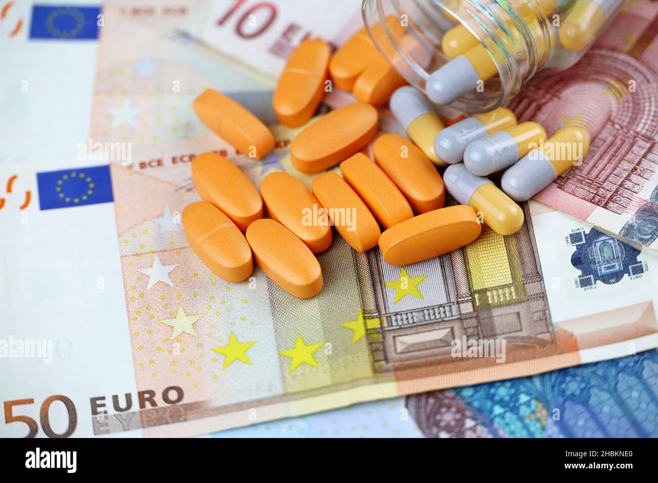 Pillole e capsule sparse da una bottiglia su banconote in euro. Concetto di assistenza sanitaria in UE, commercio farmaceutico, prezzi dei farmaci, farmacia Foto Stock