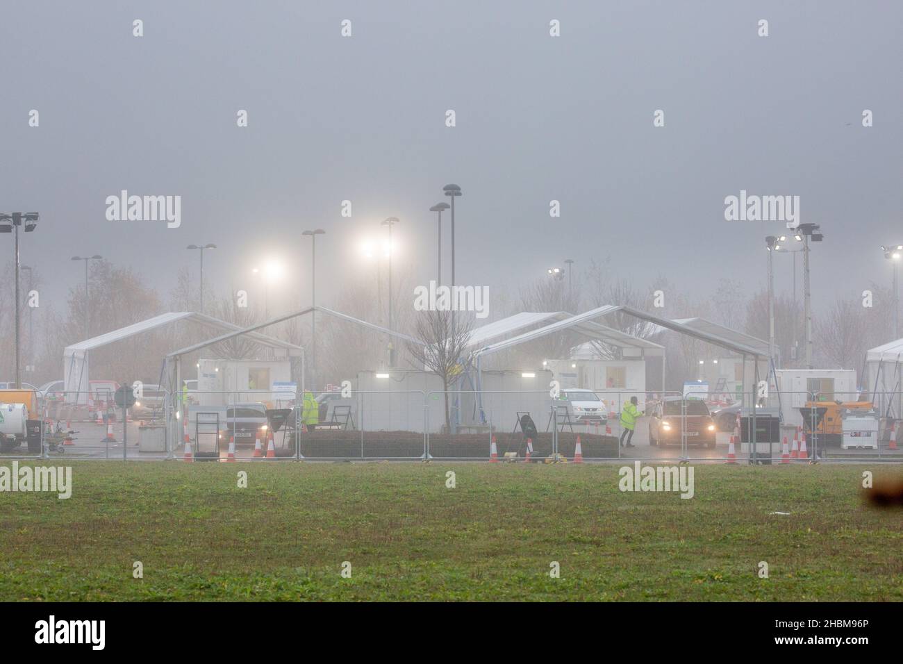 La foto datata Dicembre 19th 2021 mostra l'affollata strada covid attraverso il centro di test a Milton, Cambridge, sotto i riflettori su una nebbia Domenica mattina come la gente andare per i loro test PCR. Con l'aumento dei casi Omicron, la domanda di test è in aumento e alcune persone non sono in grado di prenotare uno slot per un test o ottenere kit di test a casa. Foto Stock