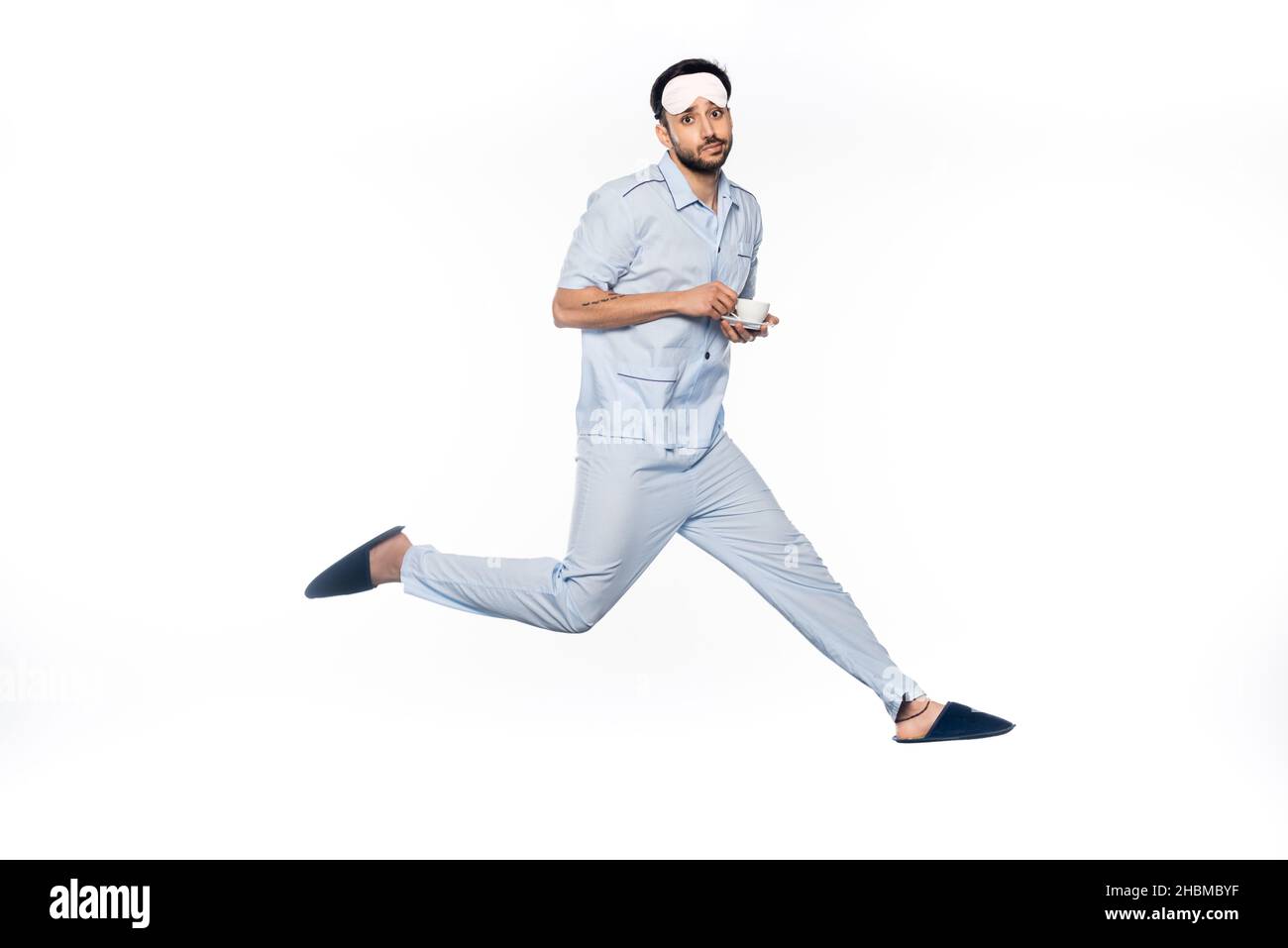 l'uomo bearded in pigiama che tiene la tazza ed il piattino mentre levitating su bianco Foto Stock