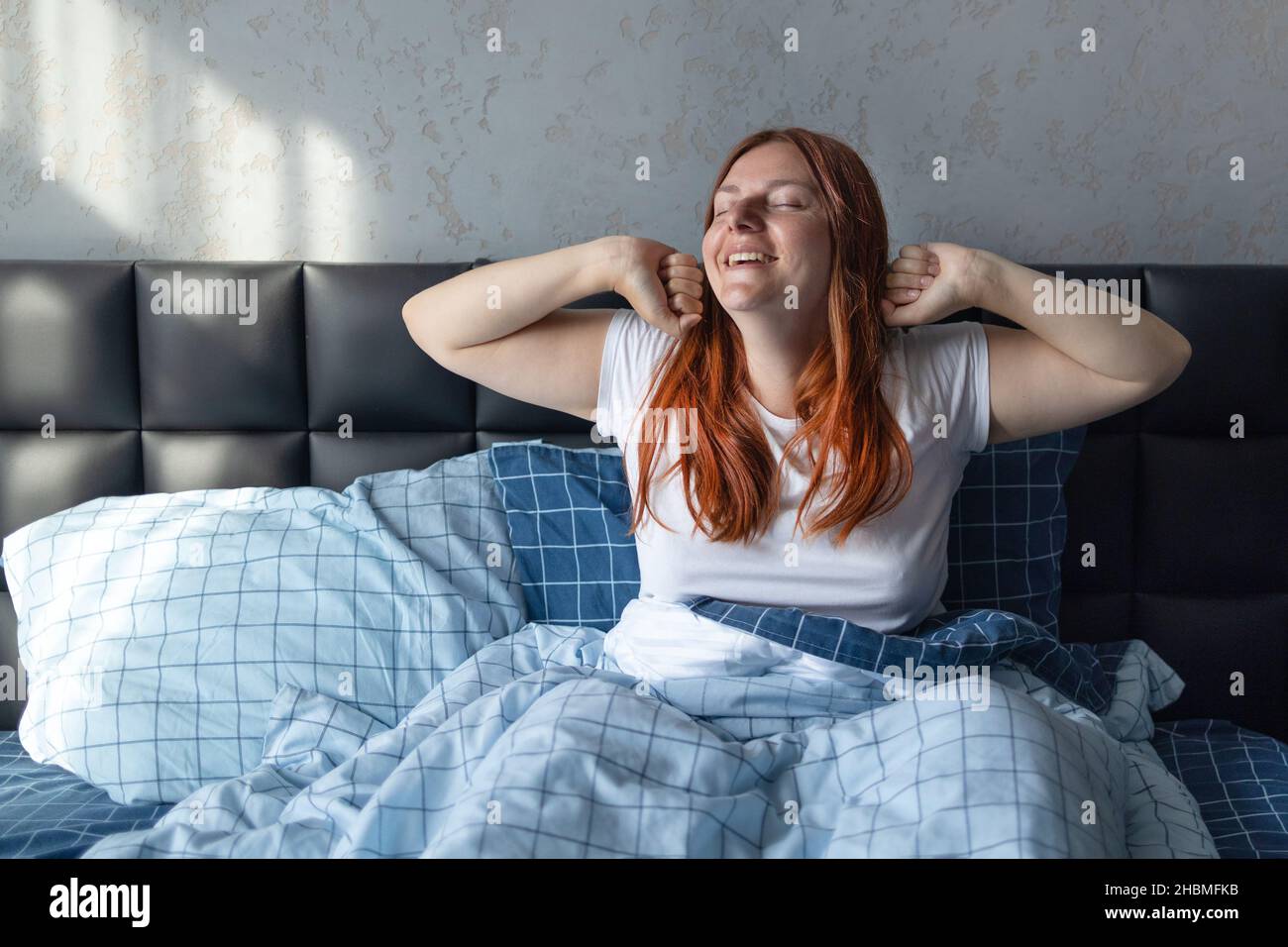 Giovane donna felice che sbava e stretching in un letto confortevole a casa. Risveglio precoce, non dormire a sufficienza, concetto di sonno eccessivo Foto Stock