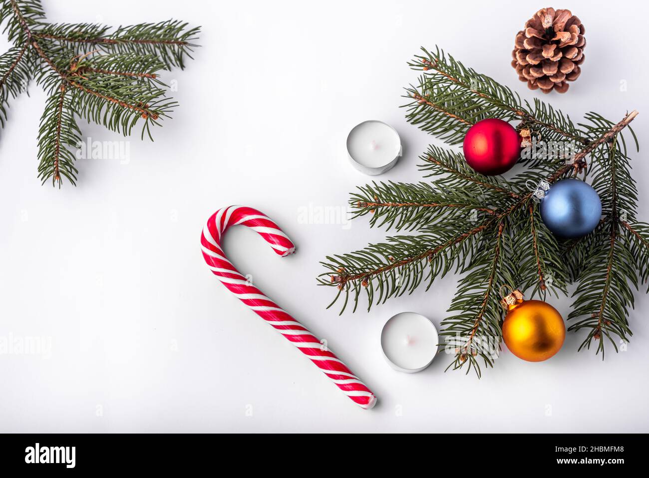 Natale e nuovo anno piatto laici: Ramo di abete verde, cono, rosso, blu e giallo palle, due candele e caramello caramella su sfondo bianco isolato. Foto Stock