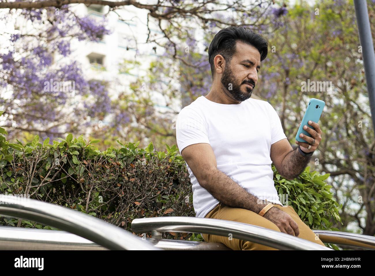 Un uomo ispanico di mezza età seduto su una struttura tubolare in acciaio e inviare un messaggio Foto Stock