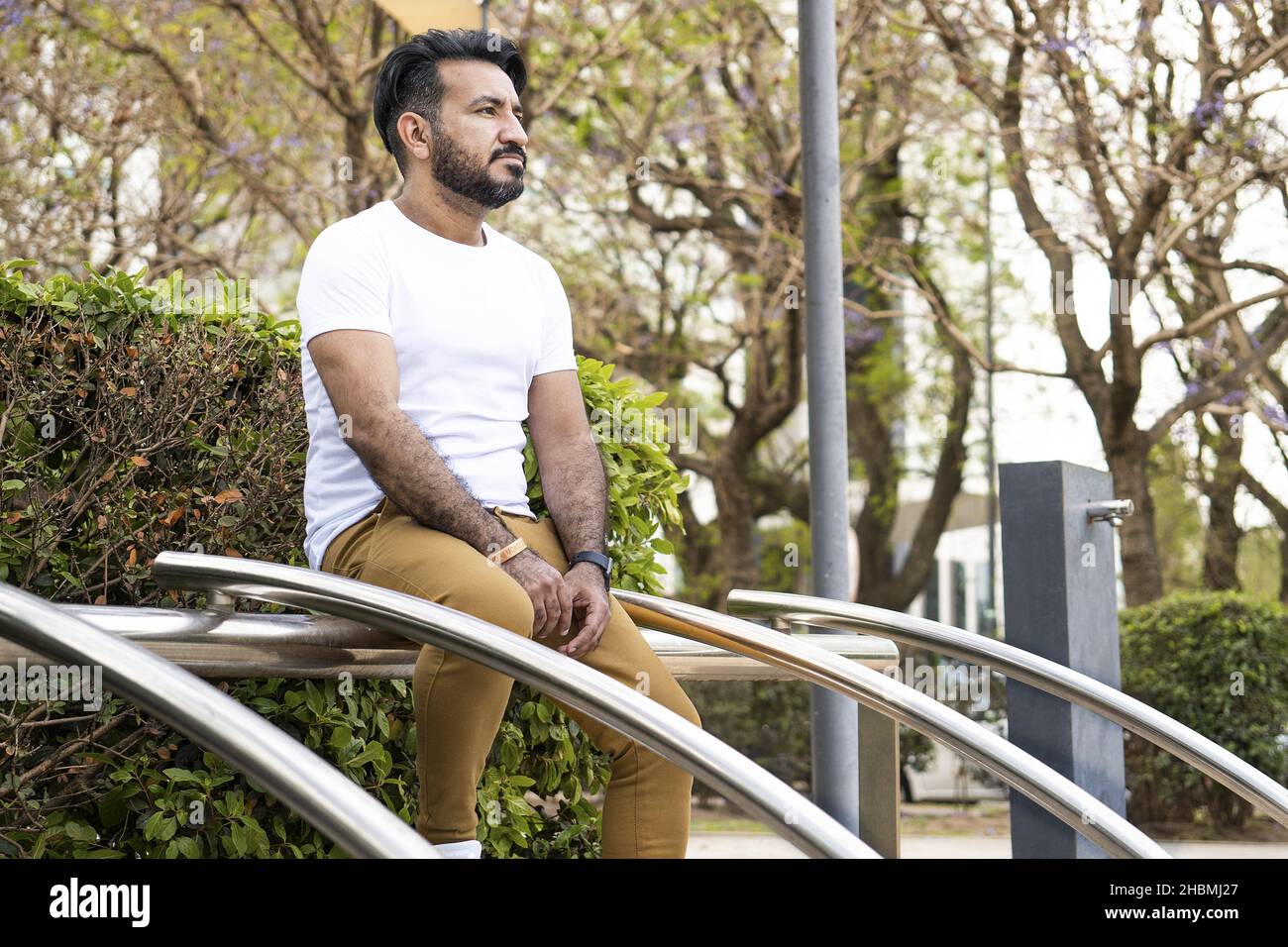 Un uomo ispanico di mezza età seduto su una struttura tubolare in acciaio in un parco Foto Stock