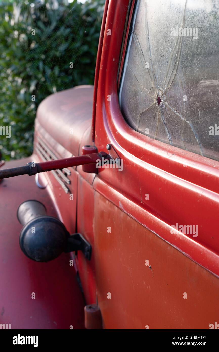 Vista laterale del vecchio pick up rosso della metà del 20th secolo con un buco proiettile e crepa nella porta del finestrino dell'auto. Concentratevi sul foro della pallottola a destra Foto Stock